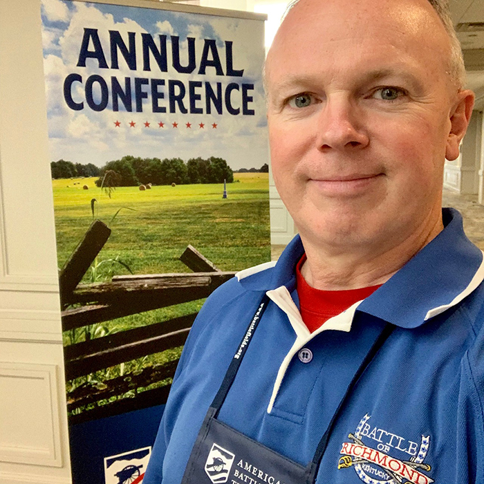 Man infront of a banner reading "Annual Conference"